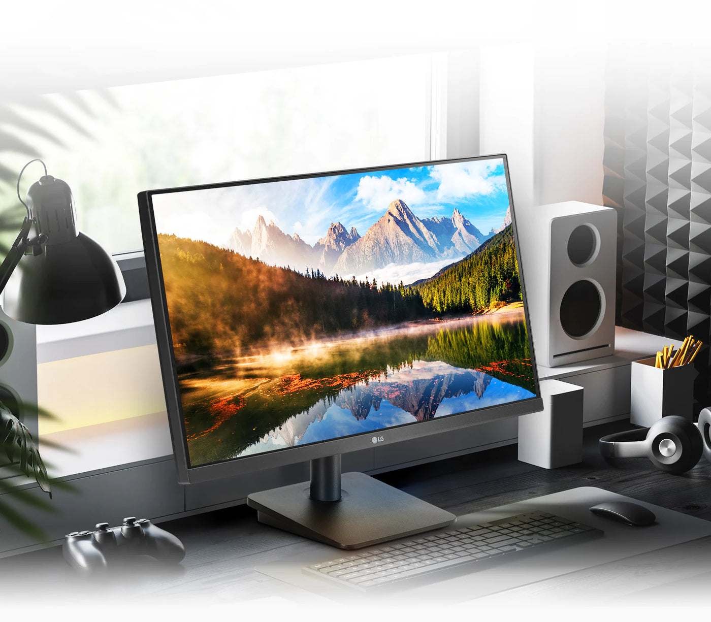 LG 24MP400-B monitor a kijelzőn hegyes völgyes, vízparti tájkép. Művirágok, egér, fejhallgató, joystick és billentyűzettel egy asztalon otthoni környezetben.